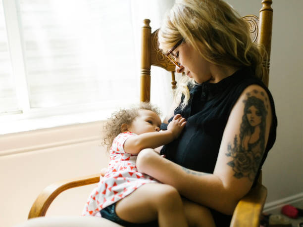 Maman qui donne le sein à sa fille de deux ans sur une chaise en bois